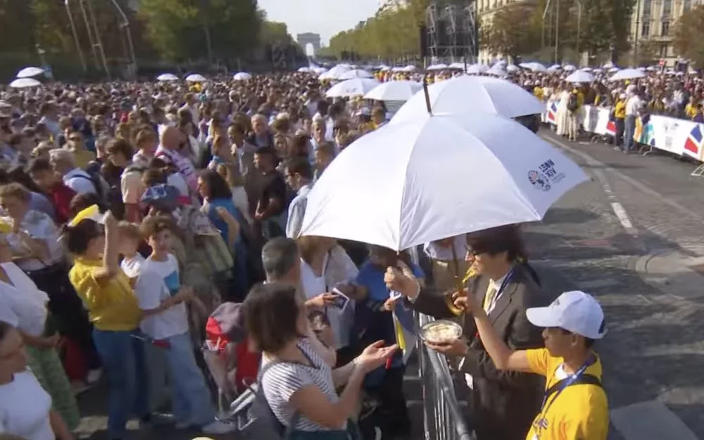 Distribution de la communion sous un parapluie personnalisé Léon XIV lors de la messe sur les Champs-Élysées